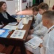 A scientist points to a worksheet with children in lab coats listening to what she is saying