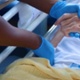 Image is a close-up of two people holding hands in a hospital setting.