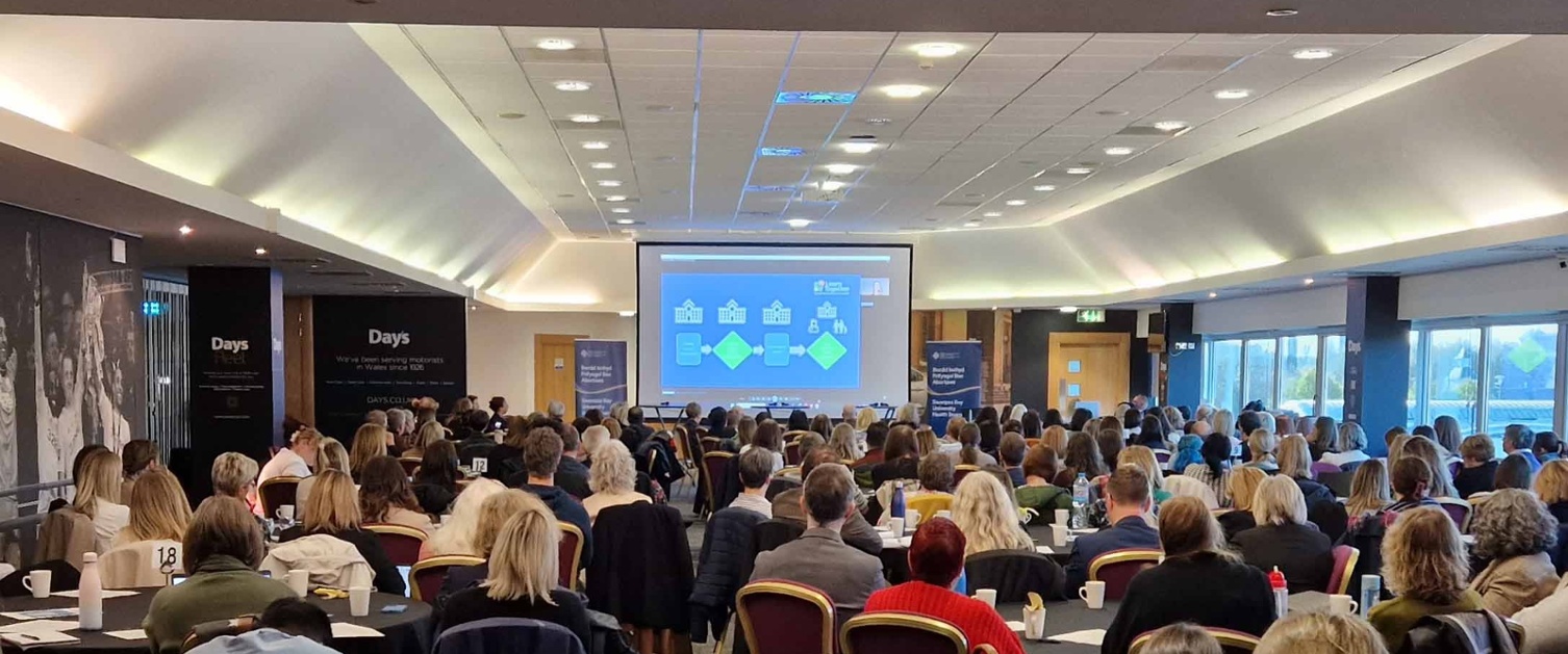 Image shows a large group of people at a conference.