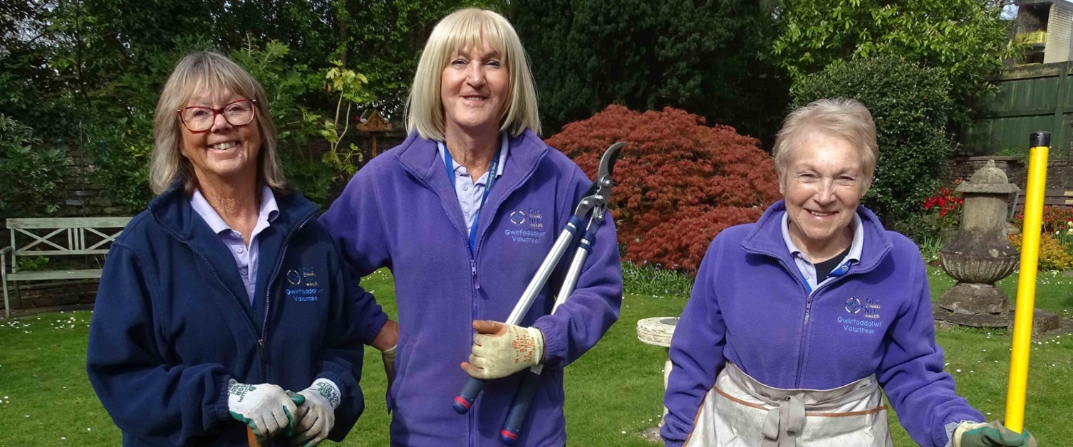 Image shows three volunteers standing in a garden.
