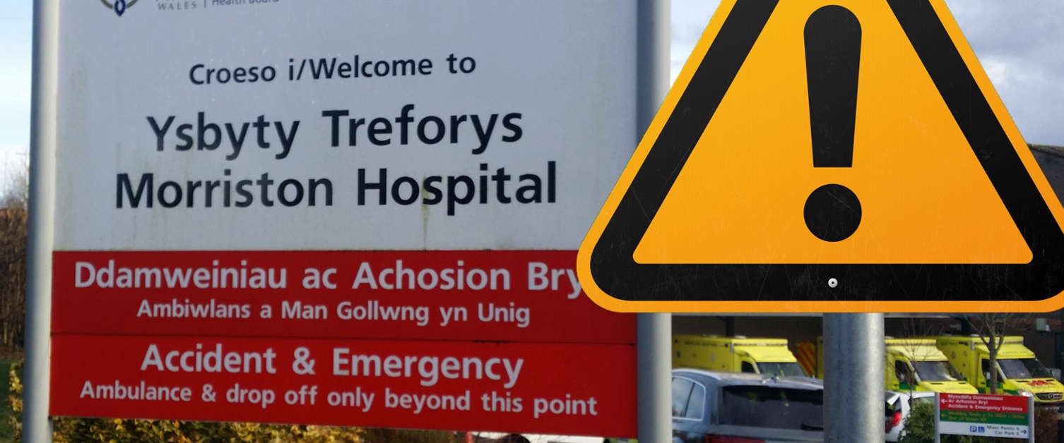 A sign outside Morriston Hospital with a warning sign in front of it.