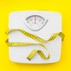 Image shows white weighing scales with a yellow measuring tape.