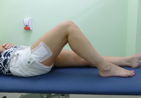 A patient lies on a bed. Their right leg is bent at the knee.