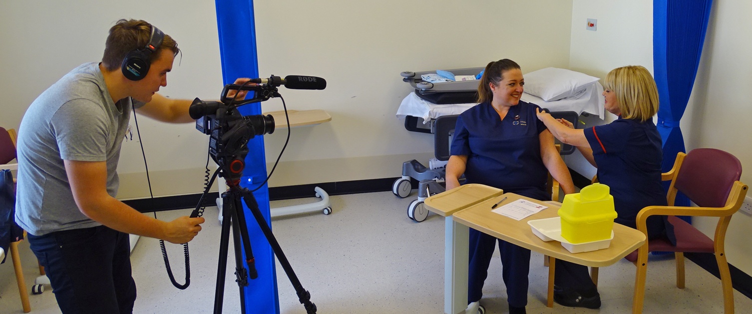 A photo of a nurse receiving her flu vaccination while being on film