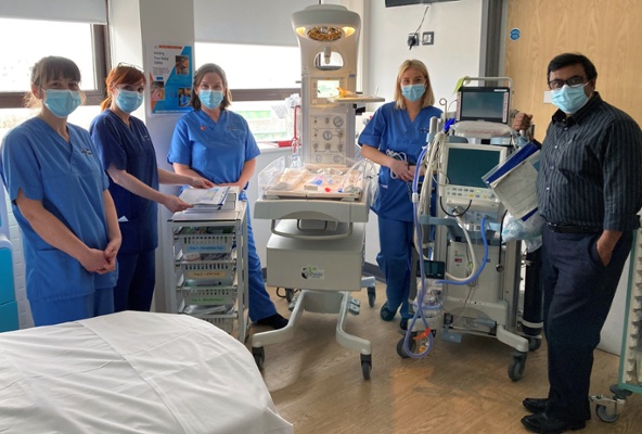 Image shows staff standing around a specialist neonatal device
