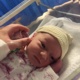 Image shows baby in hospital cot and parent holding hand.