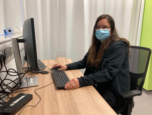 Image shows a women sat at a desk wearing a mask