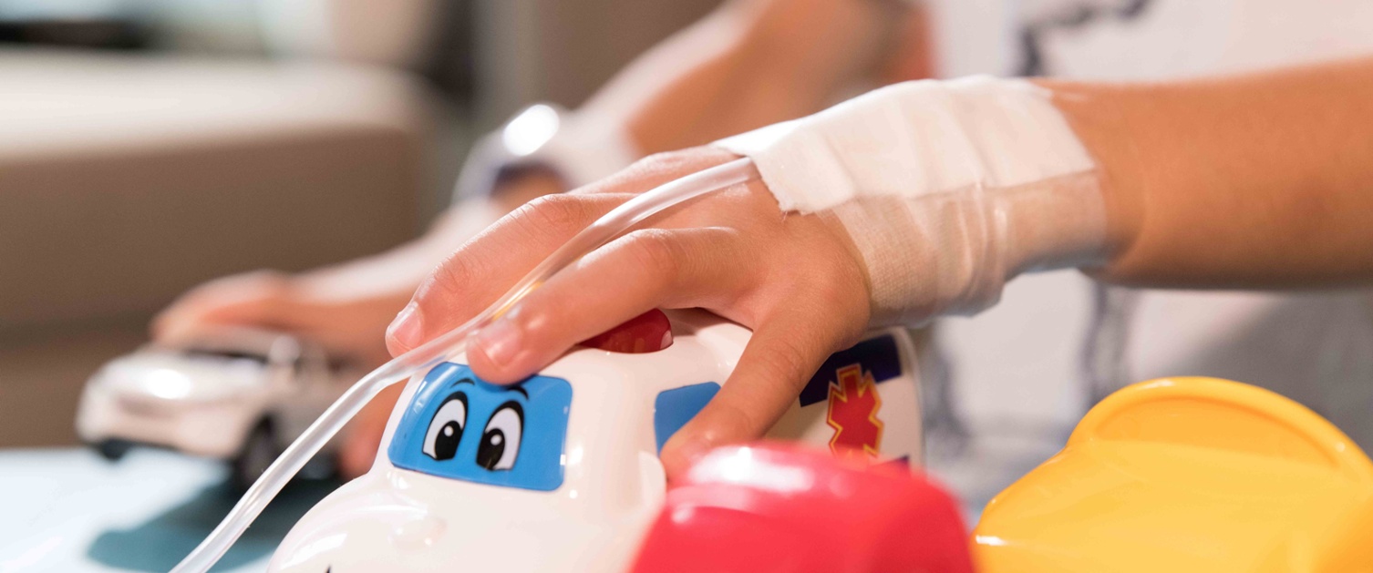 Image shows hands of a young hospital patient playing with toy cars.