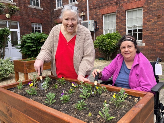 Image shows two women in front of a raised flower bed