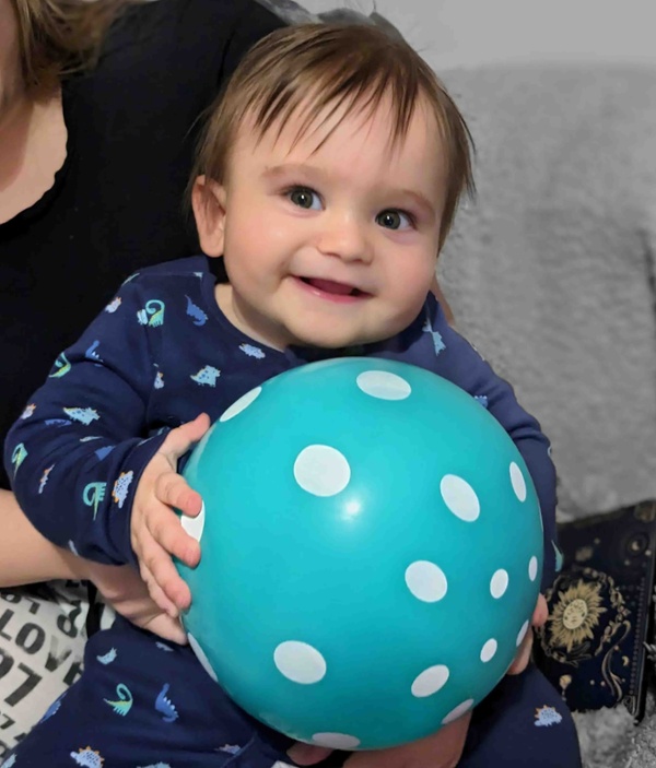 Image shows a smiling baby holding a ball.