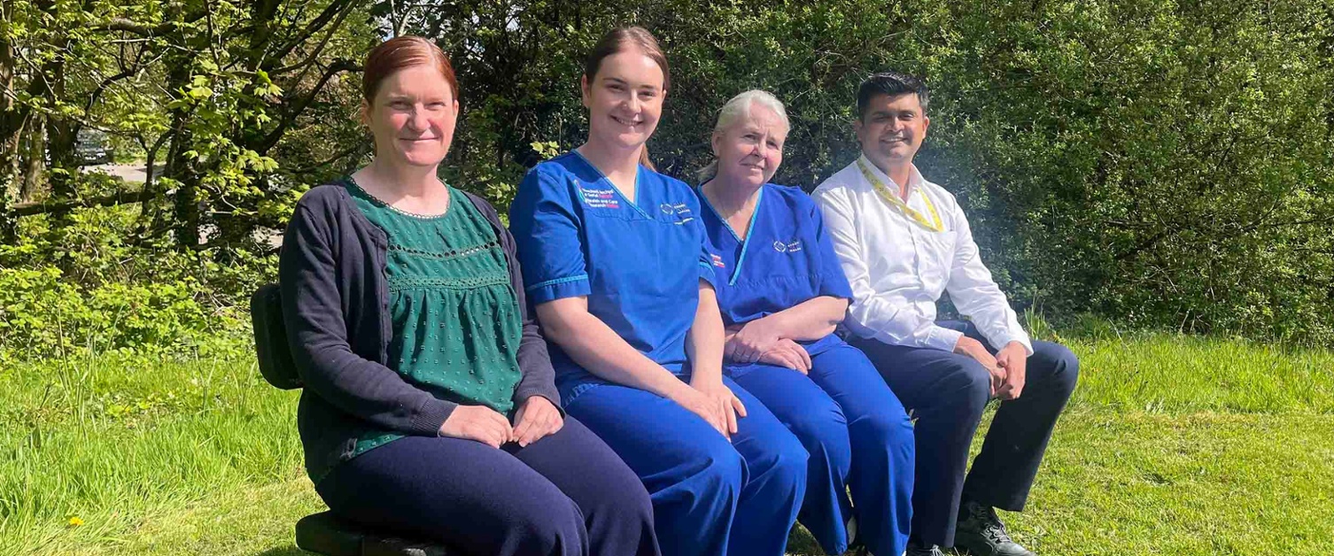 Image shows four people seated in a wooded area.