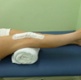 A patient is on a bed. Their right leg is raised with a rolled towel under their knee.