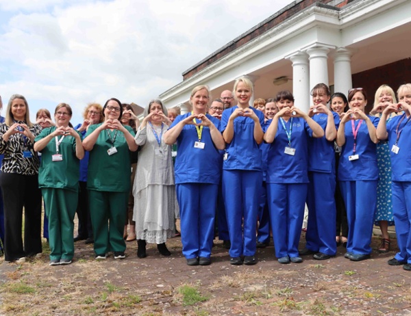 Image shows a large group of nurses in uniform making a heart shape with their hands.