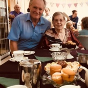 A patient sits with a porter in front of a table laden with cakes and china cups.