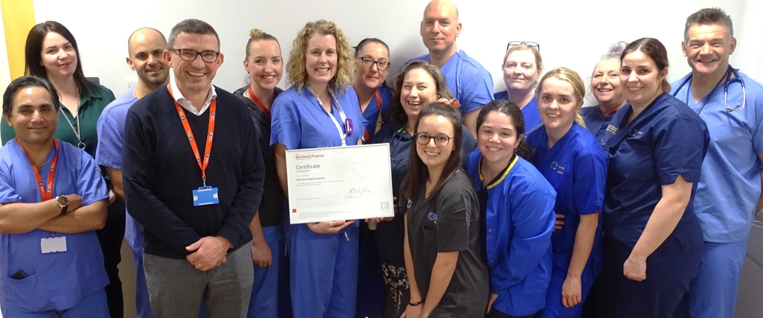 Image shows a group of smiling hospital staff with an award and celebratory cake.