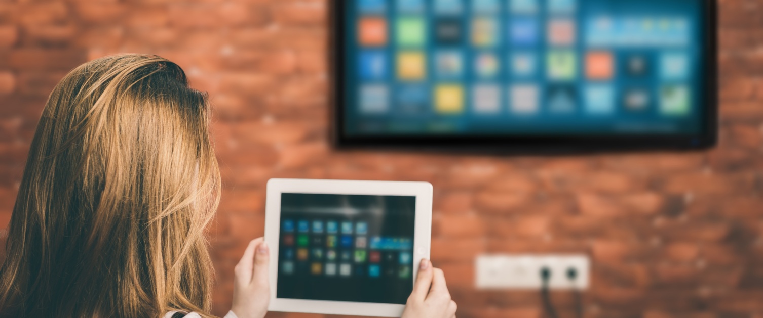 A woman looks at a tablet computer and a TV is on the wall