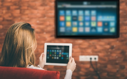 A woman looks at a tablet computer and a TV is on the wall