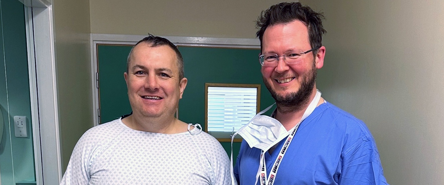 Image shows a patient with a surgeon pictured outside a hospital room