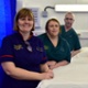 Image shows hospital staff in uniform arranged around a bed in the Discharge Lounge.