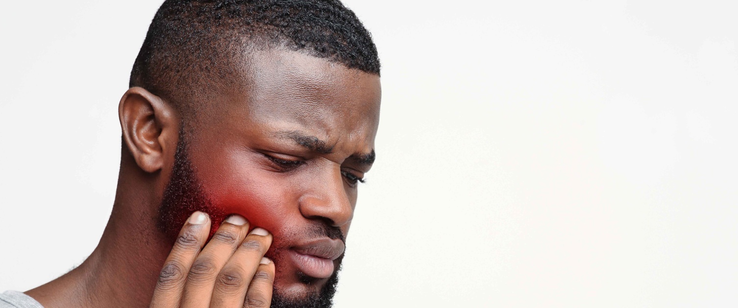 Image shows a man touching his jaw which is red to signify pain.