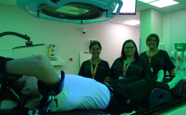 Image shows three people and a patient in a radiotherapy room