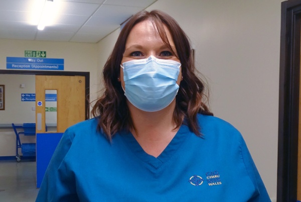 A hospital worker, wearing a mask and standing in a corridor.