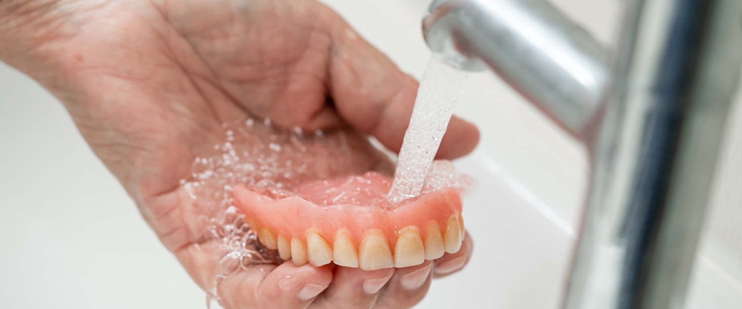 An image of someone washing dentures under a tap of flowing water