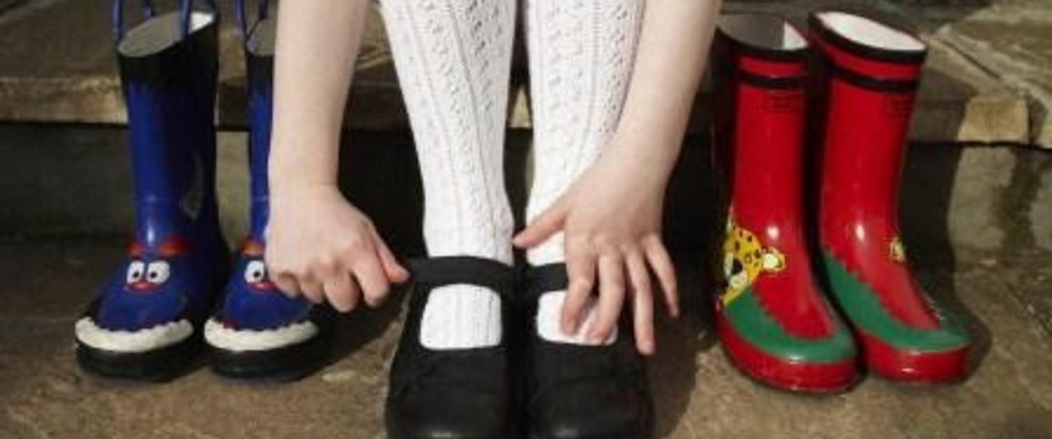 A young girl putting her shoes on, with a pair of shoes either side of her