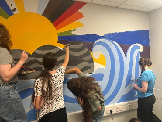 Image shows women painting a wall
