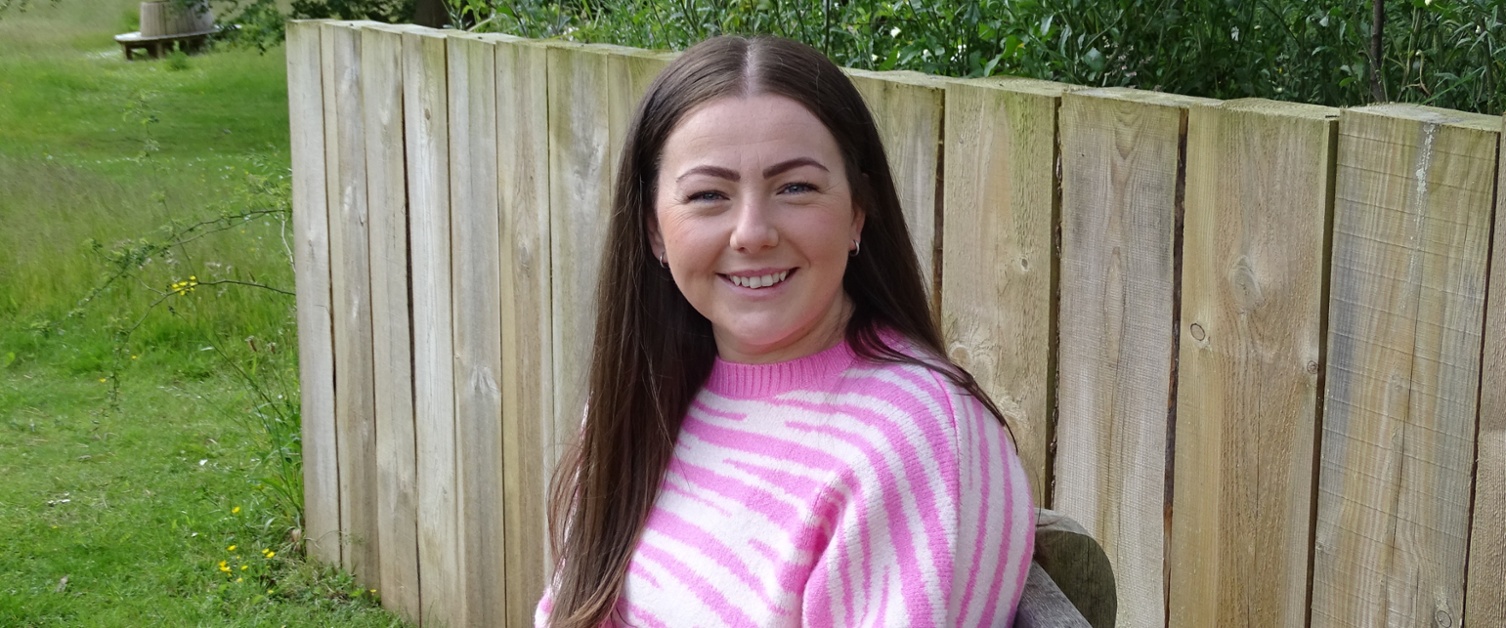 A smiling woman sitting on a bench in hospital grounds.