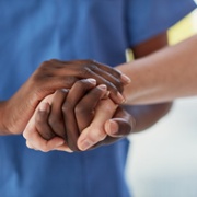 A close up of a staff member in blue scrubs holding hands with someone else.