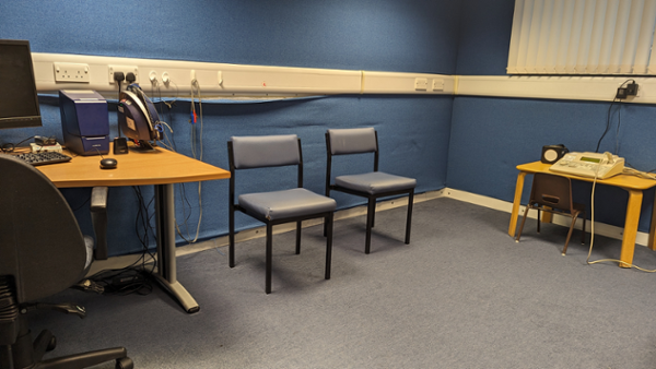 Image shows two grey chairs in front of a blue wall next to the audiologist desk.