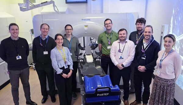 Image shows a group of people alongside a CT scanner.