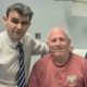 Image shows a surgeon and a nurse with a patient in a hospital room.