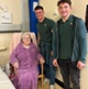 Image shows two men standing around a woman siting on a chair