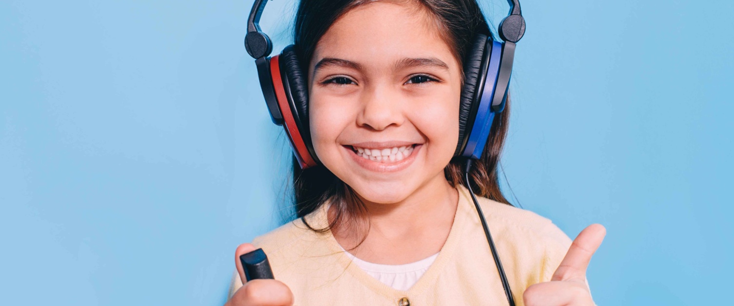 Child wearing headphones and holding button during hearing test.