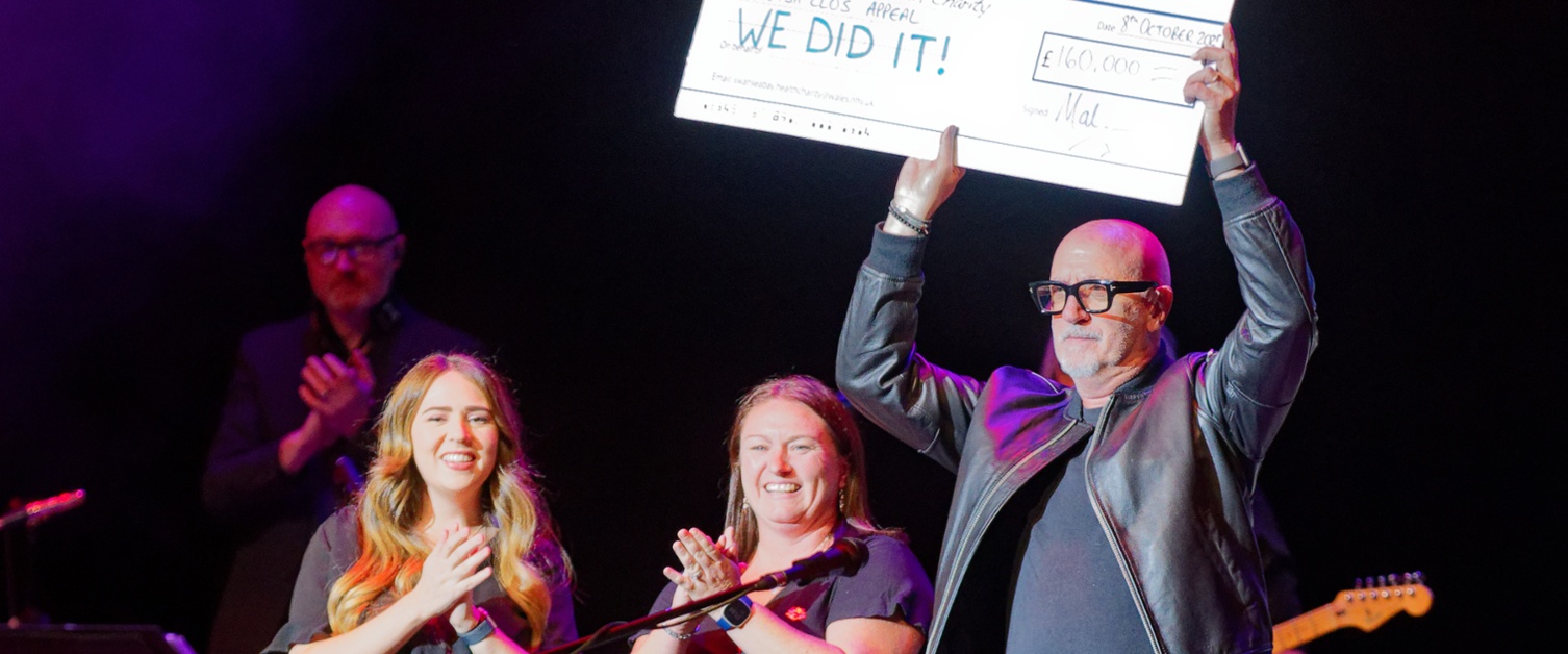 A man holding a big cheque aloft as people on stage applaud