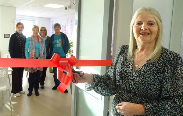 Image shows a woman cutting a ribbon to officially open a room.