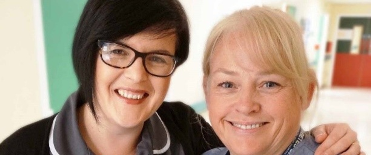 Two midwives stood together smiling at the camera holding a mug filled with treats.