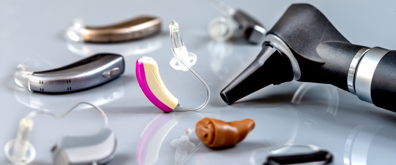 Image shows different types of hearing aids and an otoscope on a table.