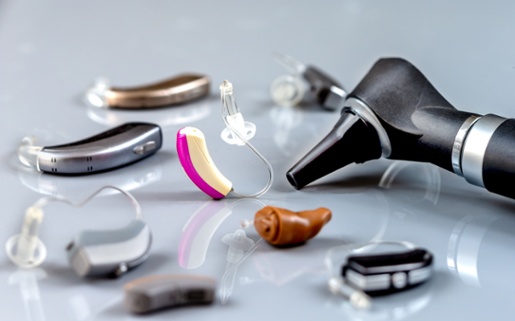 Image shows different types of hearing aids and an otoscope on a table.