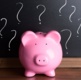 A pink piggy bank in front of blackboard with question marks.