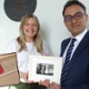 Image shows two people holding a small framed painting.