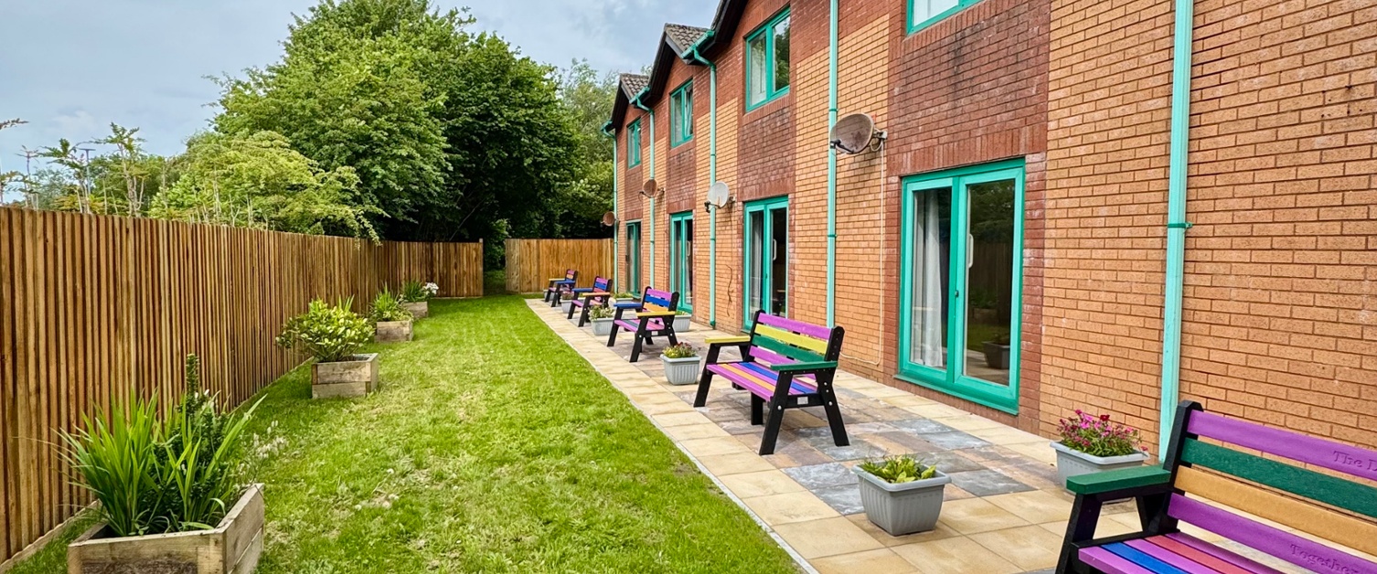 A view of a row of gardens with patios and colourful benches