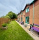 A view of a row of gardens with patios and colourful benches
