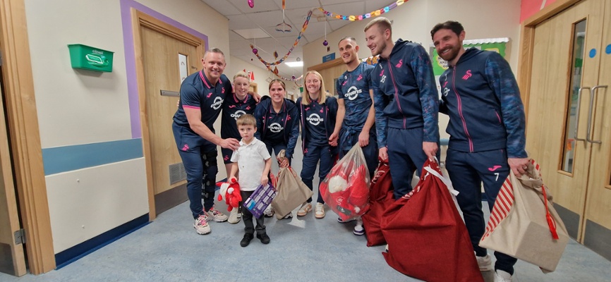 Image shows a group of people standing around a child in a hospital ward