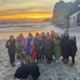 Image shows a group of women standing in a line on a beach
