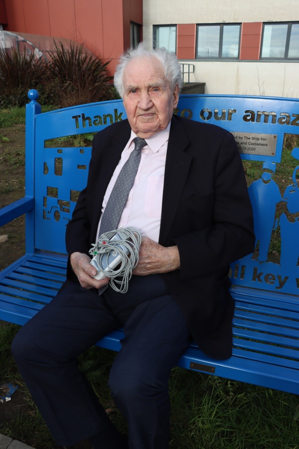 An elderly gentleman, pictured sitting outside a hospital with an item of medical equipment