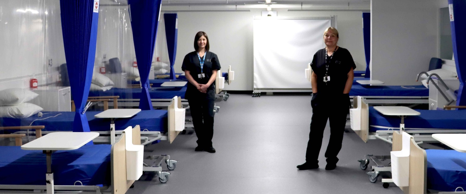 Image shows staff in scrubs stood between beds in an empty and unused ward.