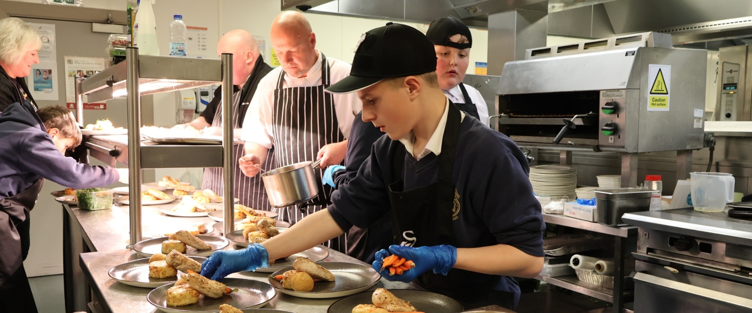 Children placing food on a plate in a kitchen